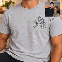 A man wearing a light heather gray t-shirt with a black line art graphic of a couple on the left chest. The image features a small inset photo in the top right corner showing the couple mentioned in the graphic.