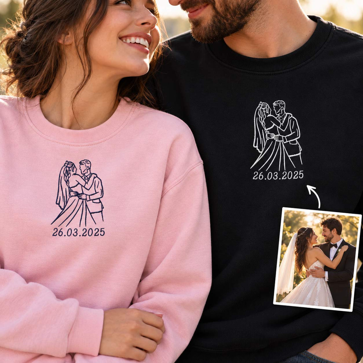 A man and a woman wearing matching personalized sweatshirts. The woman wears a light pink sweatshirt with a dark purple line art graphic of a bride and groom and the date '26.