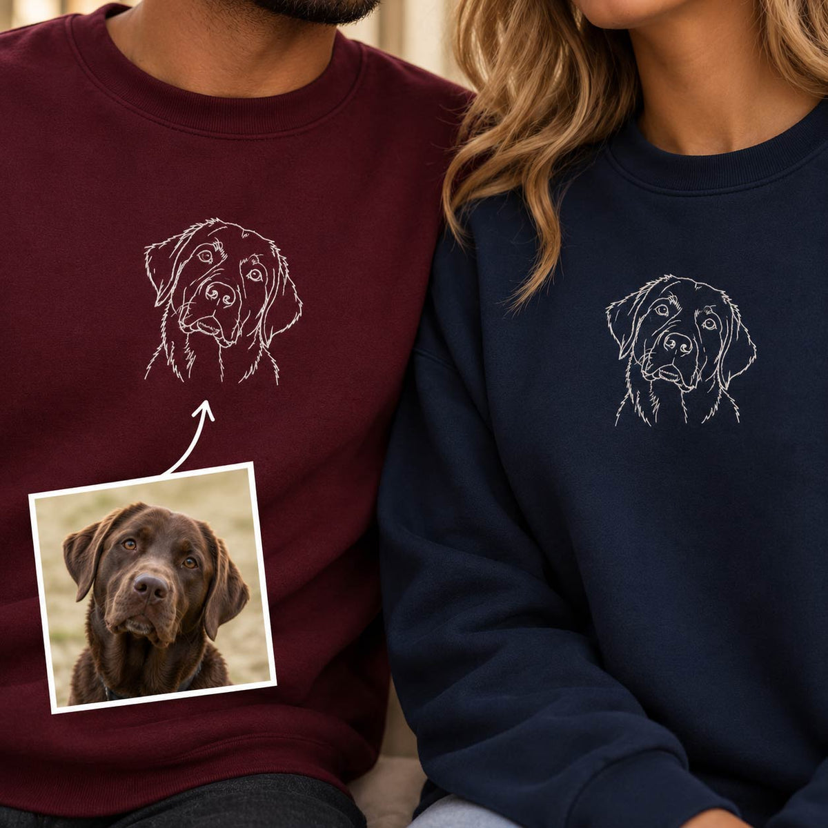 Two people wearing custom dog sweatshirts, one in maroon and one in navy blue, both featuring a white sketch of a dog on the chest. An inset photo of a chocolate Labrador retriever is shown with an arrow pointing to the custom design on the maroon sweatshirt.
