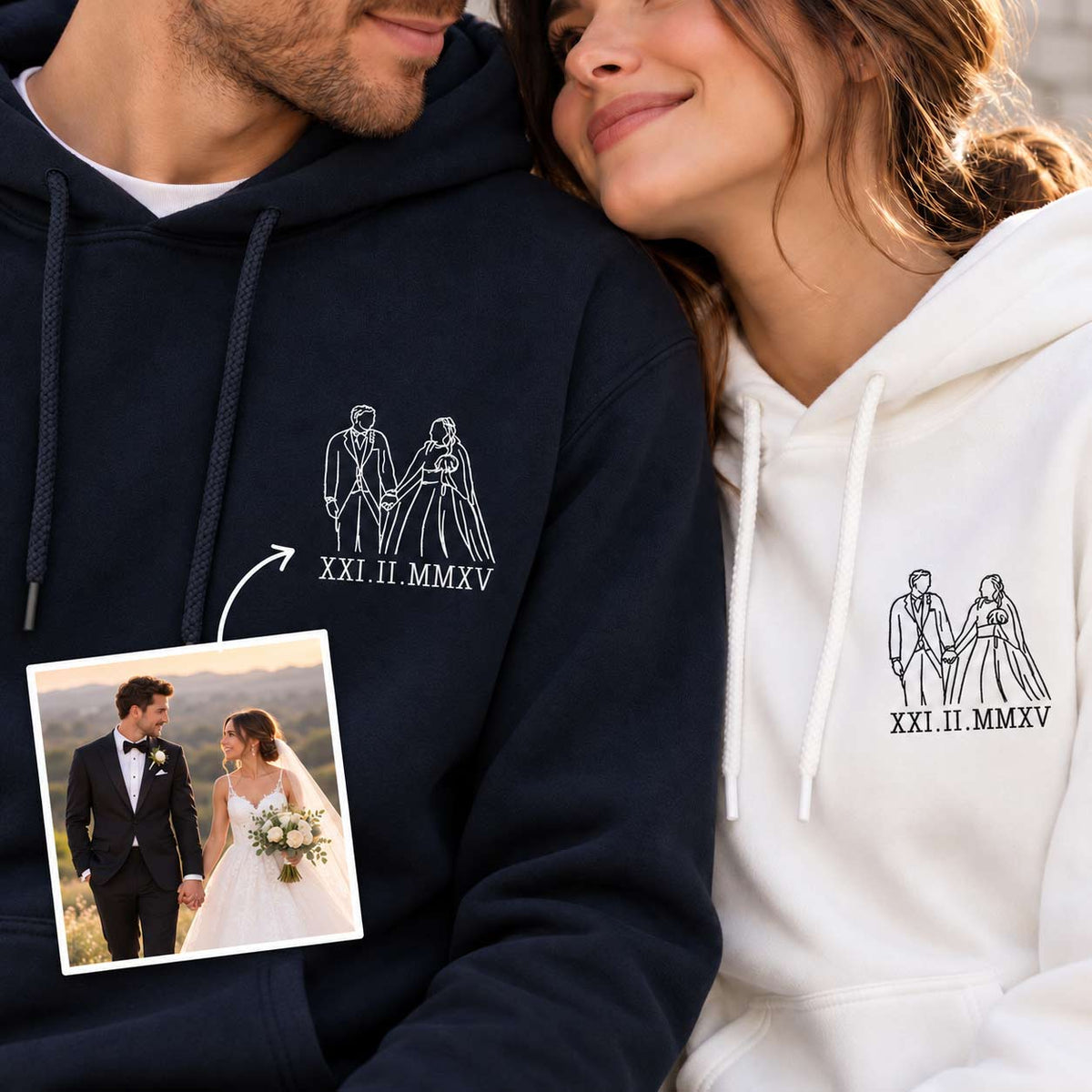 A man and a woman wearing matching custom hoodies, with the man on the left in a navy hoodie and the woman on the right in a white hoodie. Both hoodies feature a white line art graphic of a bride and groom holding hands above the Roman numerals 'XXI.