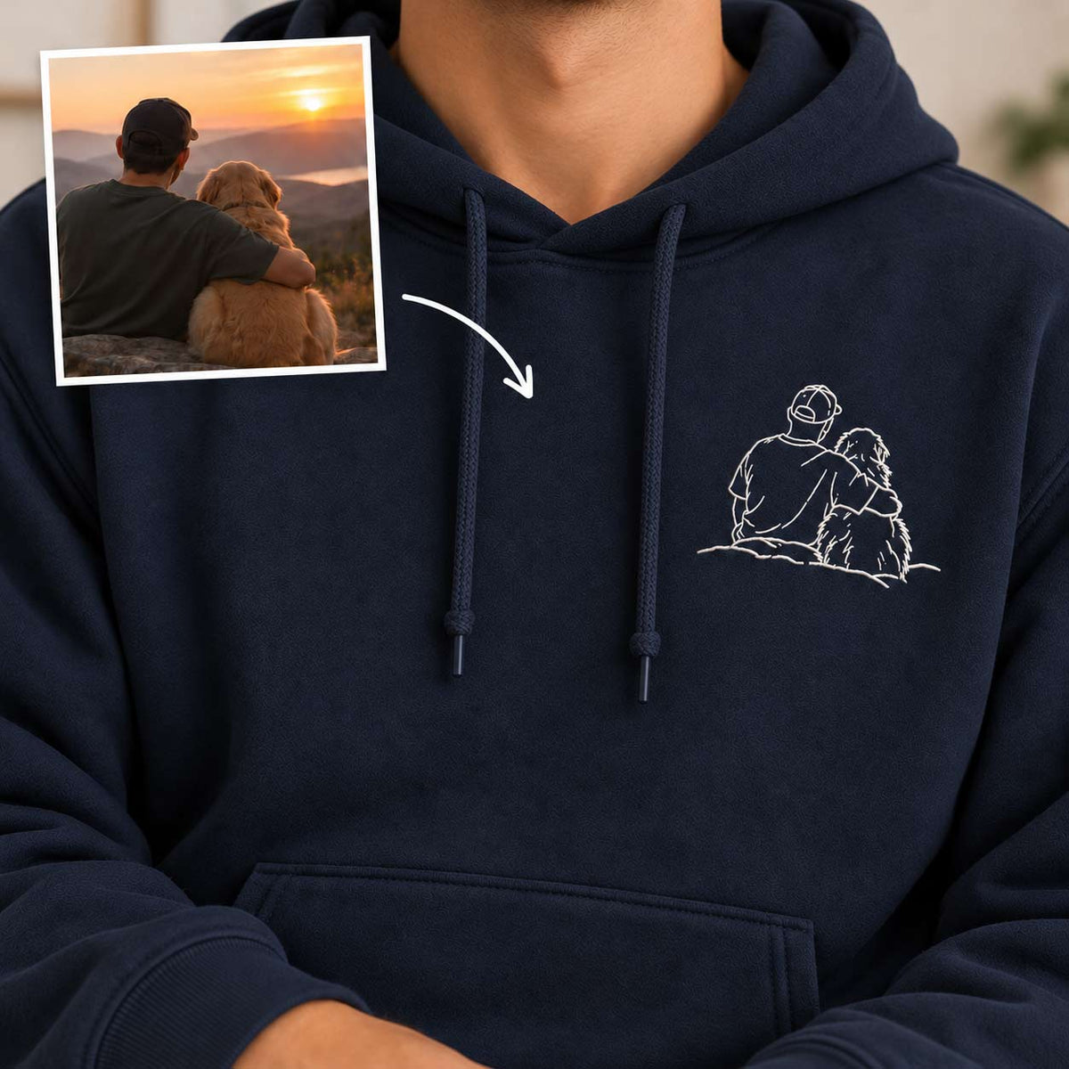 A person wearing a navy pullover hoodie with a white line-art graphic of a person and dog on the left chest. A small inset photo in the upper left shows a man and dog sitting together at sunset, with an arrow pointing to the hoodie graphic, indicating a custom print-on-demand design mockup.