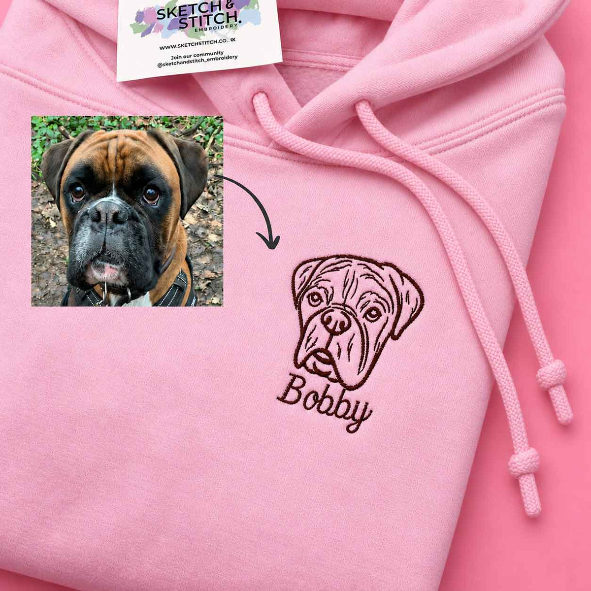A pink hoodie with a custom embroidered boxer dog face and the name 'Bobby' on the front, shown alongside a small inset photo of the original dog and a Sketch Stitch brand tag.