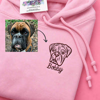 A pink hoodie with a custom embroidered boxer dog face and the name 'Bobby' on the front, shown alongside a small inset photo of the original dog and a Sketch Stitch brand tag.