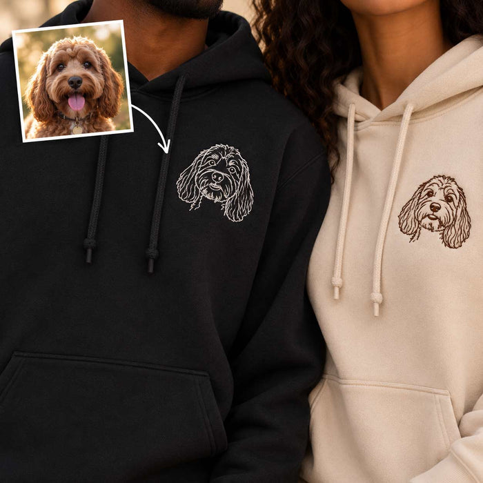 Two people wearing custom pet hoodie prints, with a small inset photo of the dog used for the embroidery design. One hoodie is black with a white dog portrait, and the other is cream with a brown dog portrait.